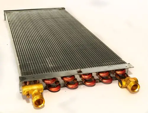 Daikin Wärmetauscher mit gerillter Oberfläche und mehreren Anschlüssen, geeignet für Heizungsanwendungen. Sichtbare Kupferrohre und Anschlussstücke aus Messing.